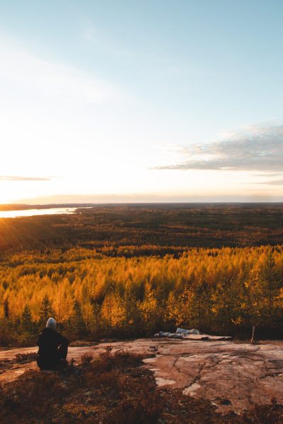 Breathtaking sunset from a rock near Paltamo, Finland. An adventurer rests on a rock and watches an orange orb illuminate the coloured leaves of the trees. Autumn colours.